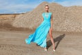 Full length portrait of a young blonde high girl in fashionable flying blue color dress poses in sand quarry