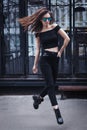 Full length portrait of young brunette girl in sunglasses jumping. Wearing checked shirt, blacg jeans and eyeglasses Royalty Free Stock Photo