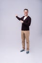 Full length portrait of a young casual man presenting something in the back isolated on gray background. Royalty Free Stock Photo