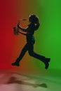 Silhouette of young girl with saxophone posing isolated on green-red background.