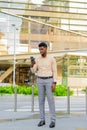 Full length portrait of young handsome African businessman in city using mobile phone Royalty Free Stock Photo
