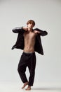 Full-length portrait of young handsome man posing shirtless in leather jacket and black pants against grey studio Royalty Free Stock Photo