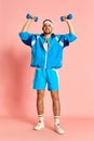 Full-length portrait of young handsome man in sportive clothes posing with dumbbells against pink studio background Royalty Free Stock Photo