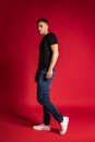 Full-length portrait of young handsome sportive man in black t-shirt and blue jeans standing alone isolated on red Royalty Free Stock Photo