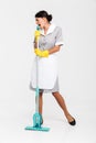 Full length portrait of young maid in gray uniform having fun while singing in mop as microphone Royalty Free Stock Photo