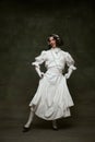 Full-length portrait of young man dressed as woman, medieval person and dancing in headphones against vintage studio Royalty Free Stock Photo