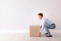 Full length portrait of young man lifting heavy cardboard box near white wall