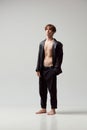 Full-length portrait of young man posing shirtless in leather jacket and black pants against grey studio background Royalty Free Stock Photo