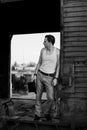 Full-length portrait of young man, wearing grey pants, white top, standing inside old railway carriage, leaning on doors. Black Royalty Free Stock Photo