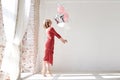 A full-length portrait of young pretty brunette woman with short curly hair, wearing red dress, doing dancing posing, holding pink Royalty Free Stock Photo