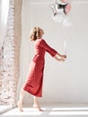 A full-length portrait of young pretty brunette woman with short curly hair, wearing red dress, doing dancing posing, holding pink Royalty Free Stock Photo