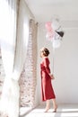 A full-length portrait of young pretty brunette woman with short curly hair, wearing red dress, doing dancing posing, holding pink Royalty Free Stock Photo