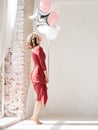 A full-length portrait of young pretty brunette woman with short curly hair, wearing red dress, doing dancing posing, holding pink Royalty Free Stock Photo