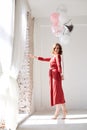 A full-length portrait of young pretty brunette woman with short curly hair, wearing red dress, doing dancing posing, holding pink Royalty Free Stock Photo