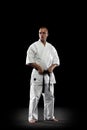 Full-length portrait of young professional karate sportsman in white kimono isolated over black background