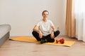 Full length portrait of young sportive girl sitting on floor on yoga mat, woman wearing black leggins and white t shirt, being