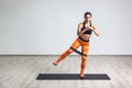 Full length portrait of young sportwoman in black top and orange leggings performs exercises for the muscles of the legs with