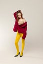 Full-length portrait of young stylish girl in yellow tights and red jacket posing isolated over grey studio background Royalty Free Stock Photo