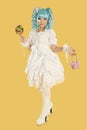 Full length portrait of young woman dressed as a doll holding lollipop over yellow background