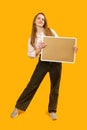 Full-length portrait of young woman with note board or cork board isolated on yellow background. Copy space