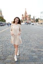 Full length portrait of a young woman with red hair, wear in beige elegant dress, behinde Kremlin red square in Moscow Royalty Free Stock Photo