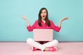 Full length portrait of young woman in rose shirt blouse white pants sitting on floor using laptop pc isolated on pink