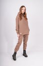 Full-length portrait of young woman in taupe hoodie and stylish coarse boots isolated on white. Beige female sweatshirt and pants Royalty Free Stock Photo