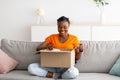 Full length of positive black lady opening cardboard package, receiving online store delivery at home Royalty Free Stock Photo