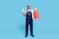 Full length positive professional courier in uniform holding shopping bags and mobile phone with mock up