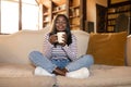 Full length of pretty black woman sitting on couch with closed eyes, enjoying cup of hot coffee, smelling aroma, indoors Royalty Free Stock Photo