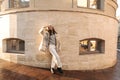 Full length pretty young caucasian lady in swoon crosses legs while standing near street building.