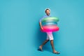 Full length profile photo of funky guy tourist walking seaside inside three colorful rubber lifebuoys swimmer wear