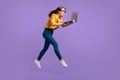 Full length profile photo of lady jump hold pc afraid look wear yellow shirt blue pants sneakers isolated violet color