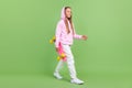 Full length profile photo of nice little blond girl hold skate go wear hoodie trousers sneakers isolated on green Royalty Free Stock Photo