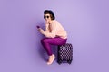 Full length profile photo of pretty lady waiting registration flight hold telephone sitting on bag wear hat sun specs Royalty Free Stock Photo