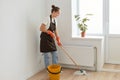 Full length profile portrait of woman housewife with bun hairstyle wearing orange rubber gloves, brown apron and jeans washing Royalty Free Stock Photo