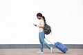 Full length profile young african american female traveler walking with cellphone and suitcase against white wall Royalty Free Stock Photo