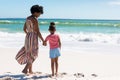 Full length rear view of african american mother and daughter holding hands while standing at beach Royalty Free Stock Photo