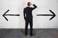 Confused Businessman Looking At Opposite Arrow Signs On Wall Royalty Free Stock Photo