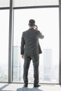 Full length rear view of mature businessman using cell phone white standing near window Royalty Free Stock Photo