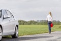 Full length rear view of woman carrying gas can leaving behind broken down car at countryside Royalty Free Stock Photo