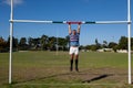 Full length of rugby player hanging on goal post at field