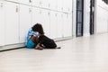 Full length of sad african american elementary schoolboy sitting by lockets in corridor