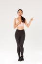 Full length of sassy attractive female athelte, asian fitness girl in sportswear pointing fingers upper right corner