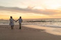 Full length of senior biracial couple holding hands while walking at beach against sky during sunset Royalty Free Stock Photo