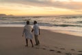 Full length of senior biracial couple walking together on shore at beach during sunset Royalty Free Stock Photo