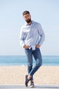 Full length serious handsome man standing by beach posing