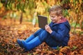 Modern day kid. Full length shot of an adorable little boy using a tablet while sitting outdoors during autumn. Royalty Free Stock Photo
