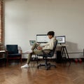 Full length shot of concentrated young male trader using online software while sitting at desk, trading online from home