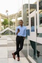 Full length shot of handsome black African businessman outdoors in city during summer smiling and holding mobile phone Royalty Free Stock Photo